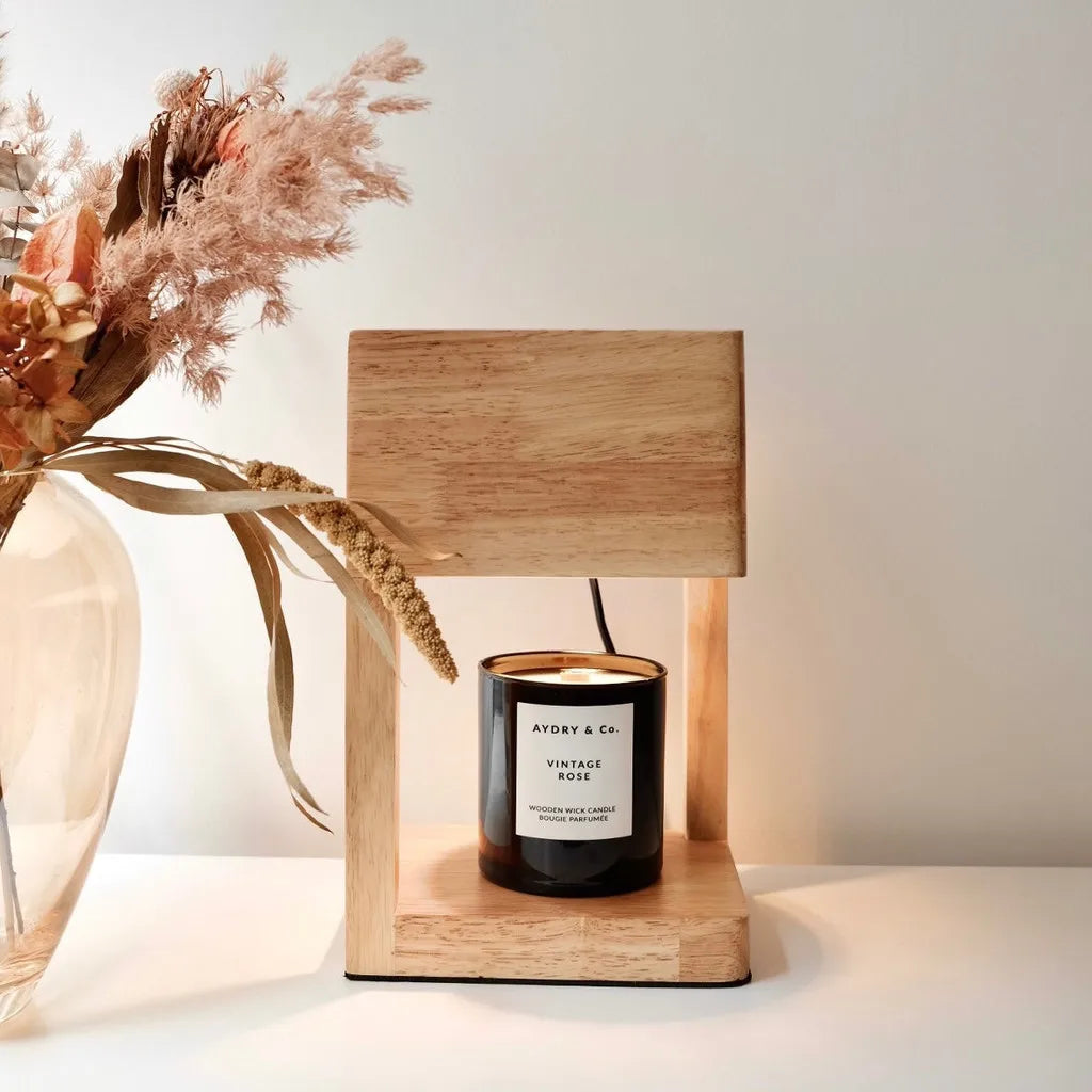 Wooden lamp with a candle labeled 'Vintage Rose' next to dried flowers on a white surface.