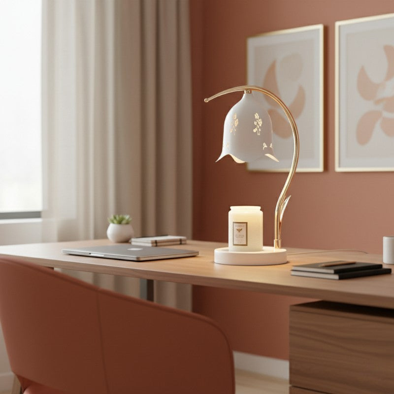 Decorative lamp on a desk with a candle, books, and a plant in a room with pink walls and framed artwork.