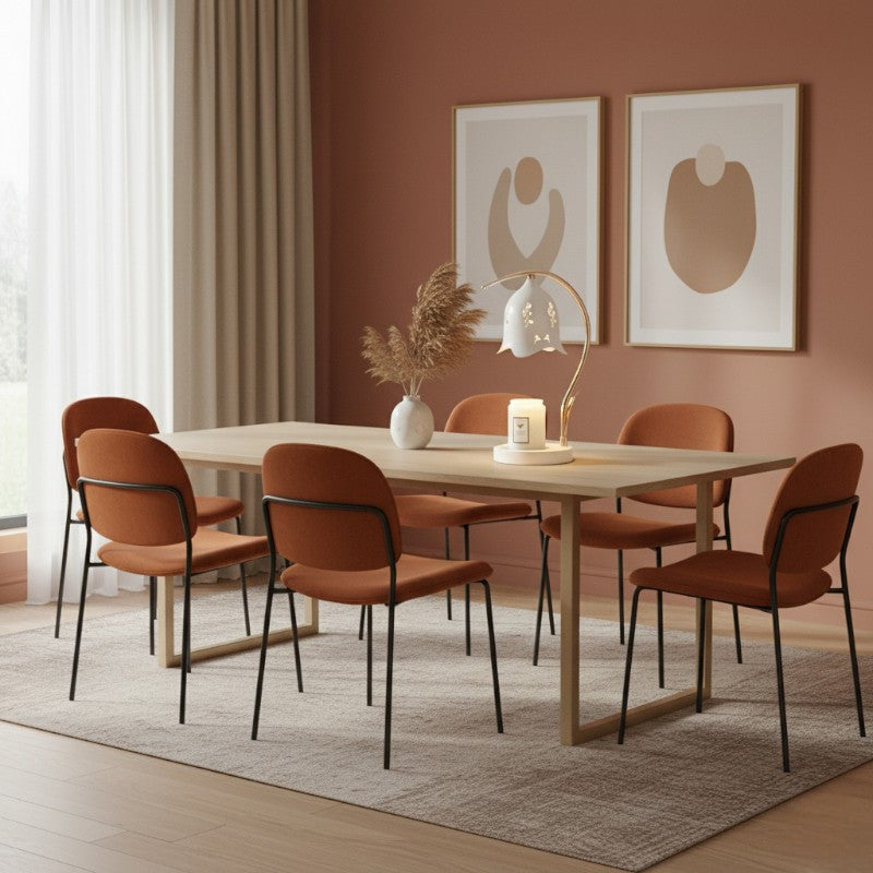 Dining room with a wooden table and orange chairs against a red wall with abstract art.